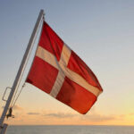Danish flag waving against a sunset over the ocean