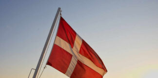Danish flag waving against a sunset over the ocean
