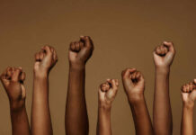 A group of diverse hands with raised fists against a brown background
