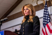 Melania Trump Hosts AI Summit: Robot Steals Spotlight A woman in formal attire speaking at a podium with an American flag in the background