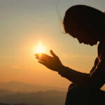 Storms to Sunshine: UK’s Wild Weather Flip Silhouette of a person in a meditative pose with hands reaching towards the sun during sunset