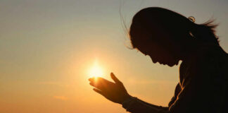 Silhouette of a person in a meditative pose with hands reaching towards the sun during sunset