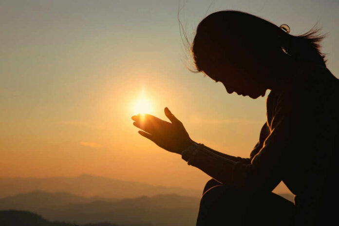 Silhouette of a person in a meditative pose with hands reaching towards the sun during sunset