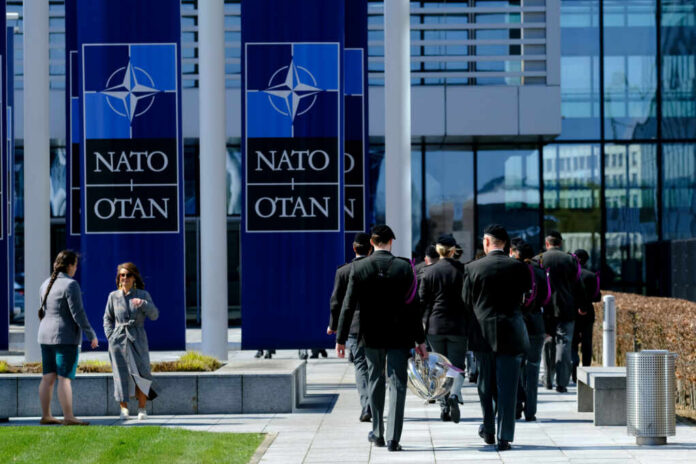 shutterstock2284726143jpg Military personnel walking past NATO banners with two women conversing in the foreground