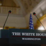 Press podium with microphones and an American flag in the background
