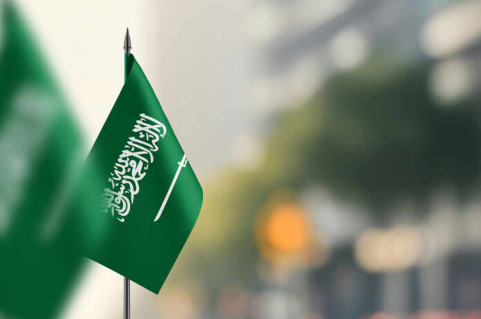 shutterstock2466834151jpg A green flag of Saudi Arabia with white Arabic text and a sword, set against a blurred background