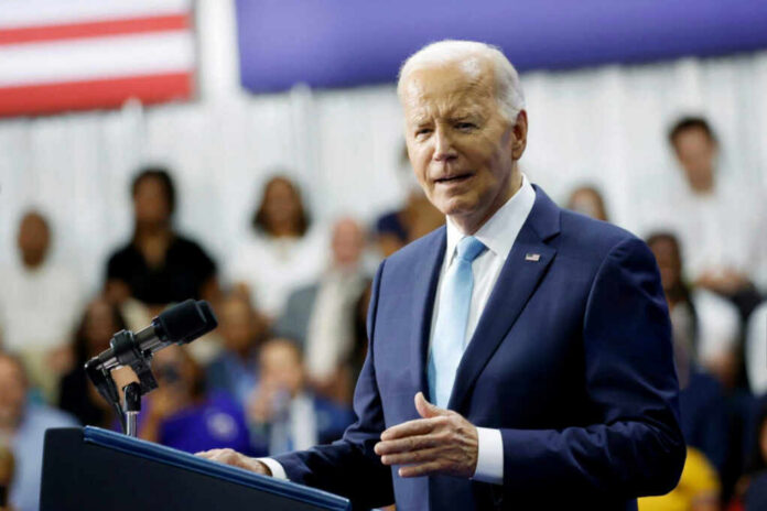 A man in a suit speaking at a podium with a microphone, an audience in the background