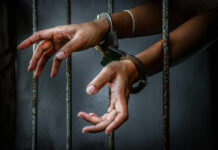 Hands in handcuffs reaching through prison bars