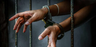 Hands in handcuffs reaching through prison bars