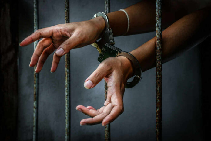 Hands in handcuffs reaching through prison bars