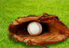 A baseball glove with a baseball resting inside, set on green grass
