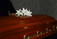 Safety Failures Led To Gulf Of Mexico Disaster A wooden casket adorned with white lilies, with a hand resting on it