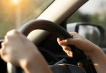 Hands gripping a steering wheel inside a car with sunlight streaming in