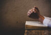 Hands clasped in prayer over an open book on a wooden table