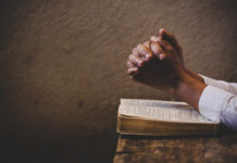Outrage Erupts Over Alleged Religious Coercion in School Hands clasped in prayer over an open book on a wooden table