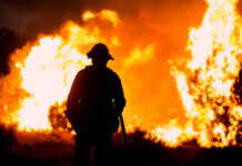 Silhouette of a firefighter standing in front of a large wildfire