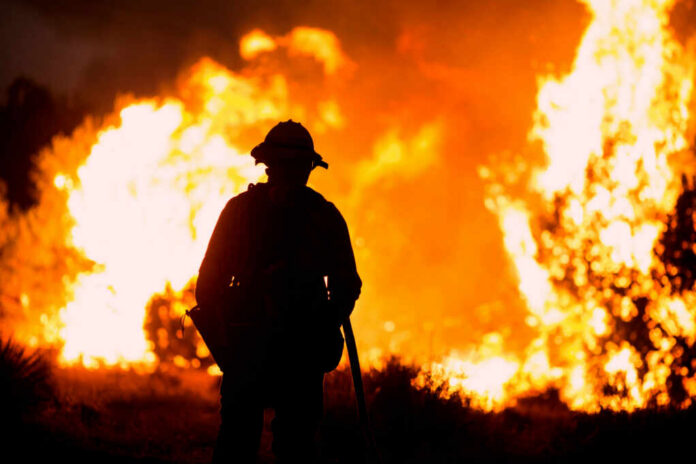 shutterstock_1818129098.jpg Silhouette of a firefighter standing in front of a large wildfire
