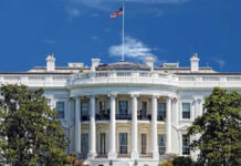The White House with an American flag flying against a blue sky