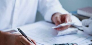 A person writing on financial documents with a calculator nearby