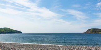 A rocky beach with colorful pebbles and a view of the ocean and green hills under a blue sky