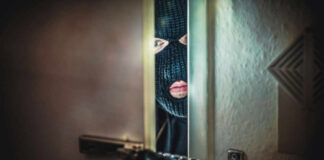 A masked intruder peering through a partially open door