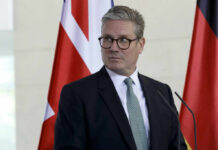 A man in formal attire standing at a podium with flags in the background