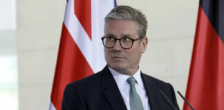 A man in formal attire standing at a podium with flags in the background