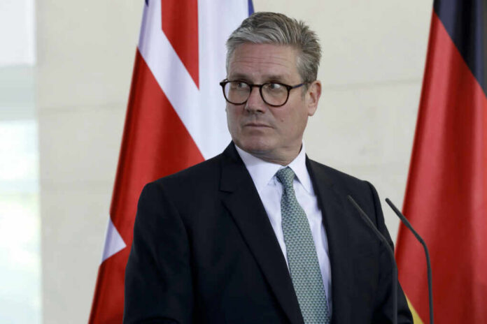 A man in formal attire standing at a podium with flags in the background