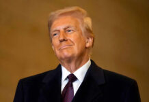 A man in formal attire smiling confidently against a neutral background