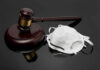 A wooden gavel next to a white face mask on a reflective surface