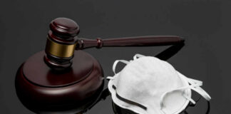 A wooden gavel next to a white face mask on a reflective surface