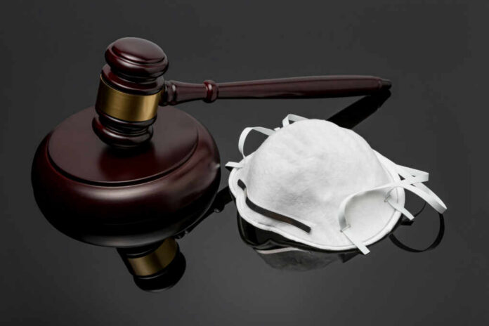 A wooden gavel next to a white face mask on a reflective surface
