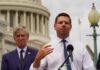 Two men at a press conference outside the Capitol building, one speaking into a microphone