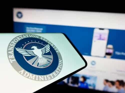 Close-up of a mobile device displaying the TSA logo with a blurred background of a website