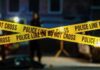 Police tape marking a crime scene with blurred figures in the background