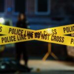 Police tape marking a crime scene with blurred figures in the background