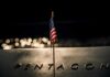 A small American flag positioned in front of the word 'PENTAGON' on a reflective surface