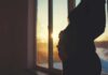 Silhouette of a pregnant woman standing by a window at sunset