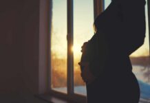 Silhouette of a pregnant woman standing by a window at sunset