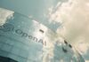 A modern glass building with the OpenAI logo against a cloudy sky