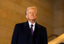 A man in formal attire standing confidently indoors with a serious expression