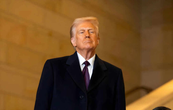 A man in formal attire standing confidently indoors with a serious expression