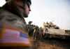Soldiers in military gear coordinating near armored vehicles during training