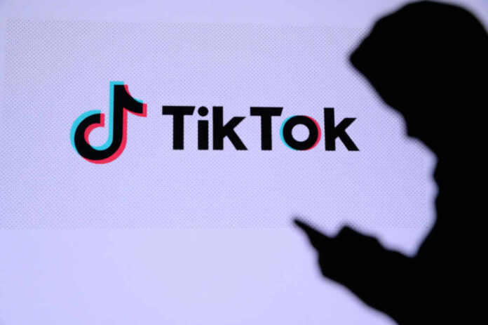 shutterstock1743989522jpg Silhouette of a person using a mobile device in front of the TikTok logo