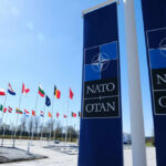 NATO Rattled: U.S. Troops Withdrawn NATO flags displayed in front of the NATO headquarters under a clear blue sky