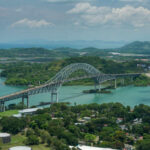 Four Nations Collide on One Bridge Aerial view of a bridge spanning over turquoise water surrounded by greenery