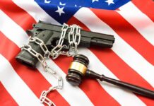 A handgun chained and placed on an American flag with a gavel nearby