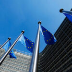 European Union flags flying in front of a modern building against a clear blue sky