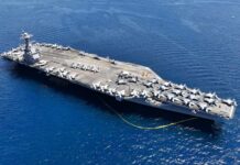 An aircraft carrier with numerous fighter jets on its deck in the ocean