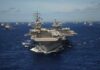 An aircraft carrier surrounded by various naval ships in the ocean